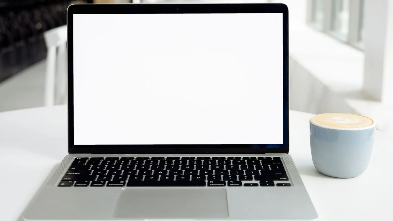 A minimalist indoor workspace featuring a blank laptop screen and a cappuccino in a modern setting.
